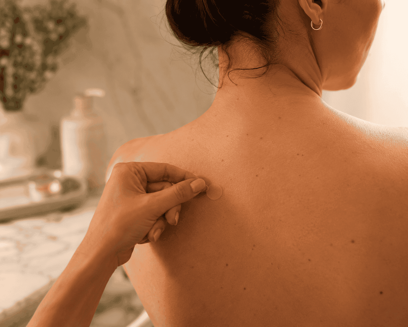 Person applying a hydrocolloid acne patch to a reachable spot on their upper back